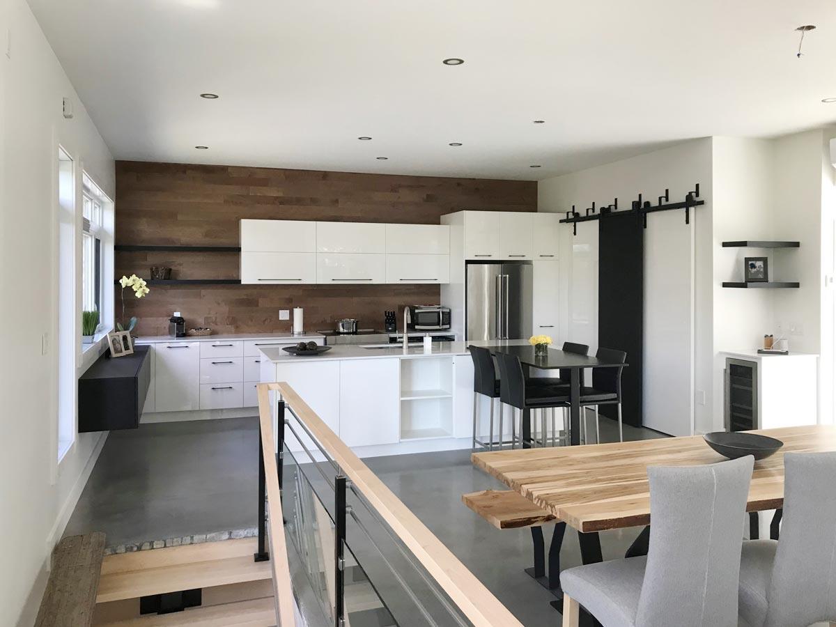 Modern open-concept kitchen and dining area featuring white cabinetry, wood accent wall, island, and a barn door.