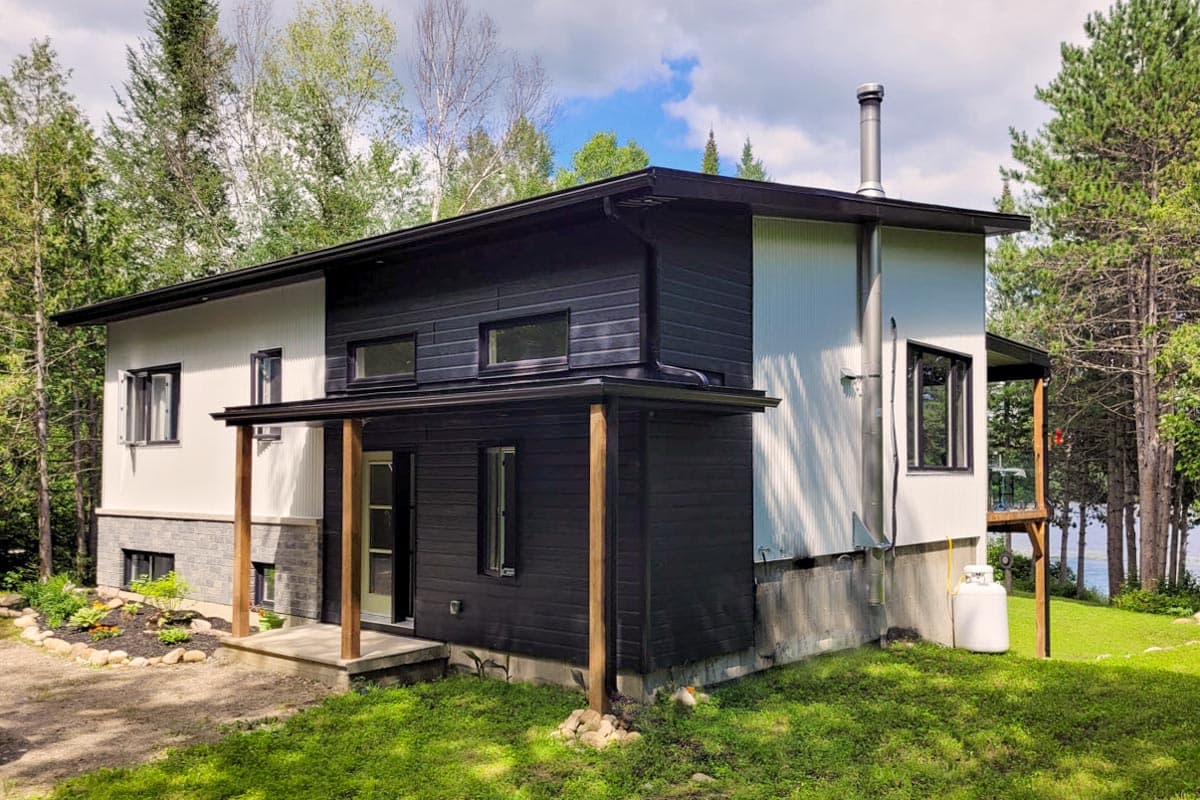 Modern house plan exterior with dark horizontal siding, white corrugated siding, and exposed wooden posts supporting a covered entrance.