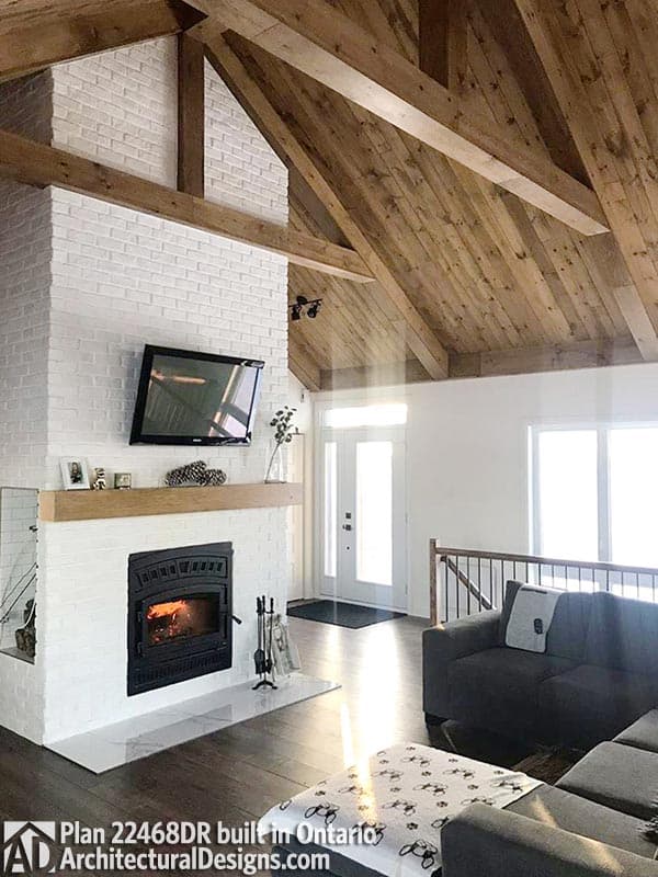 Great room with vaulted wood-beamed ceiling, white brick fireplace with wood mantel, and entry foyer.