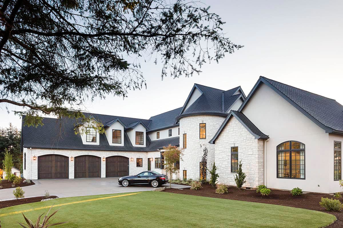 House plan exterior with a multi-story design, featuring a three-car garage, stone accents, dormers, and a round turret.