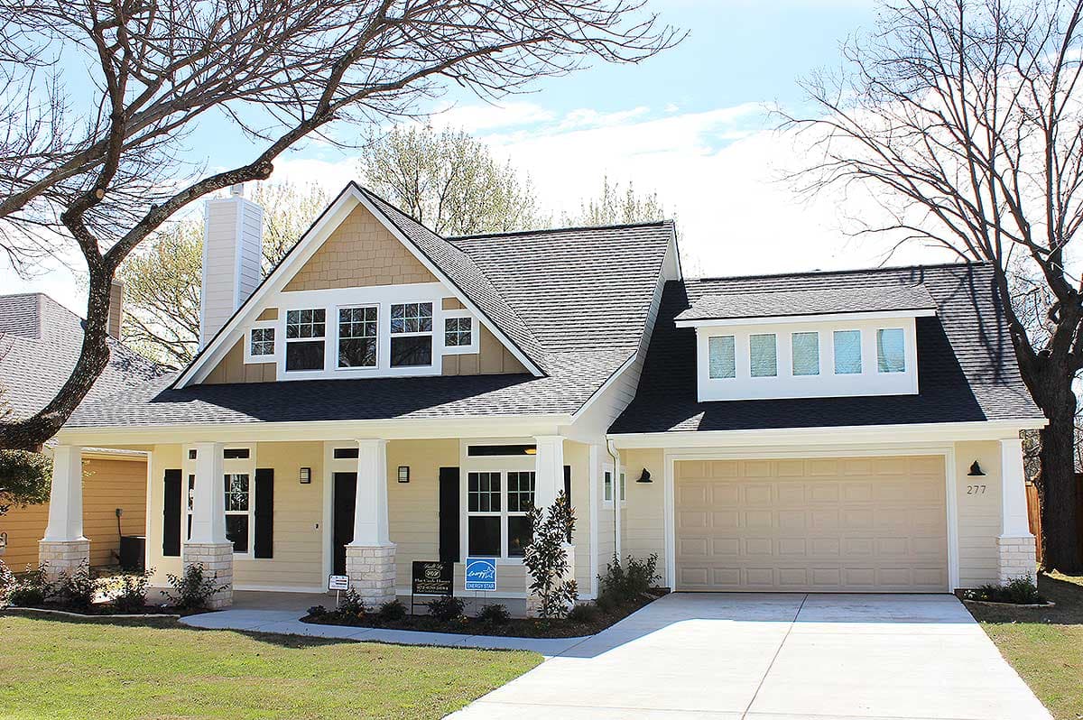 House plan exterior: Gable roof, dormer, covered porch with stone accents, and a two-car garage.