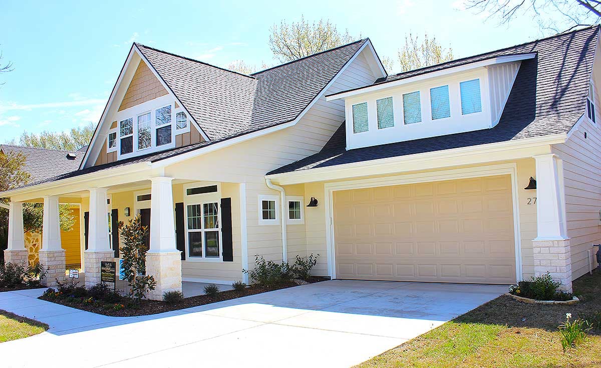 House plan exterior featuring a wraparound porch, gable dormers with multiple windows, and a two-car garage.