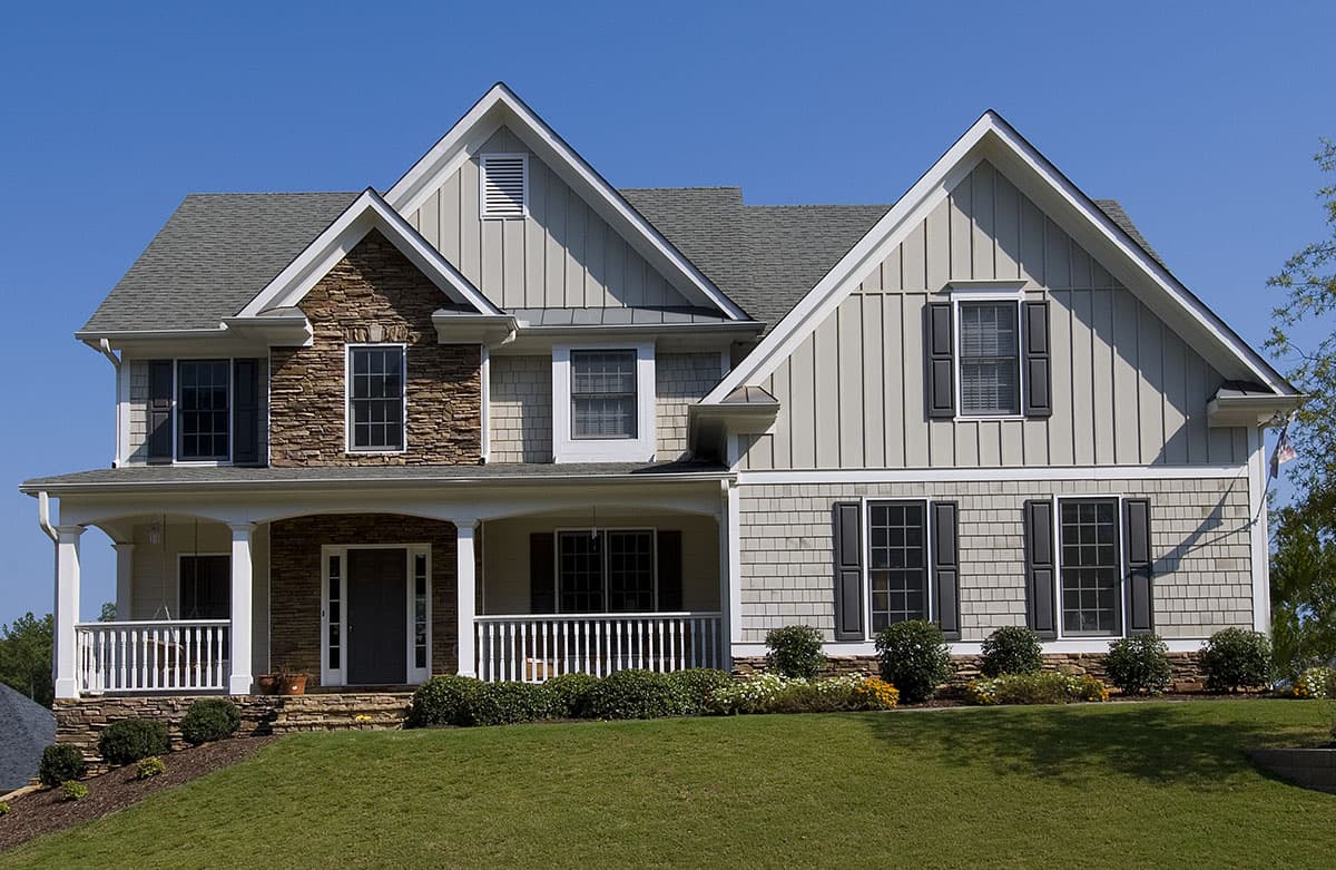 House plan exterior. Two-story home with a porch, gabled rooflines, stone and shingle siding. Front entry has a columned porch.