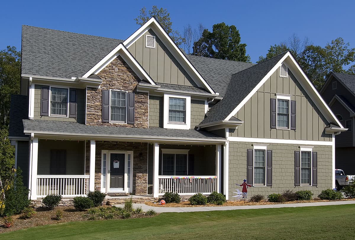 House plan exterior: Two-story home with a wraparound porch, stone accents, gable dormers, and varied rooflines.