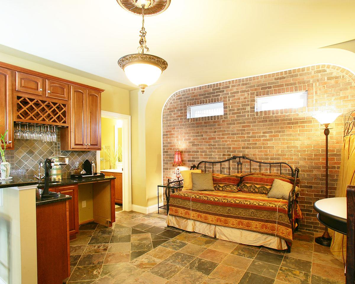 Interior view of a room with a wet bar, daybed, and arched brick accent wall with two small windows.