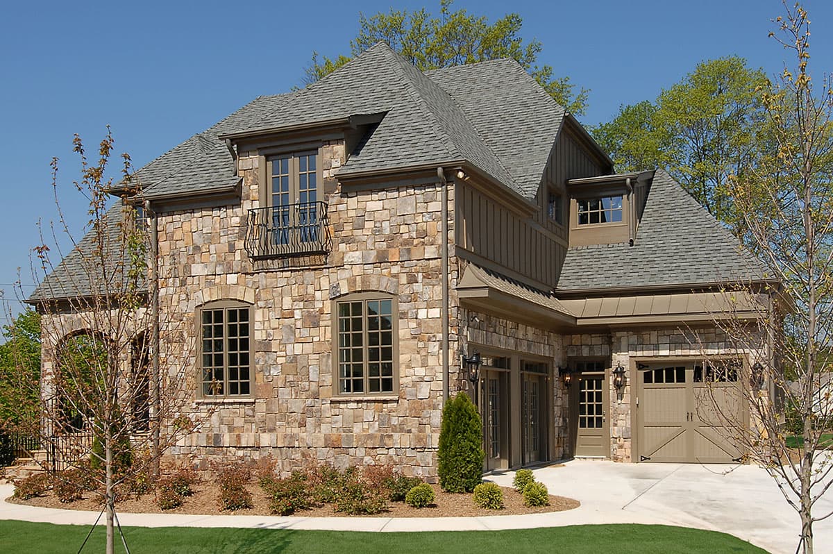 House plan exterior with stone veneer, multiple gables, dormer, and attached garage. Two stories with a balcony and arched doorway.