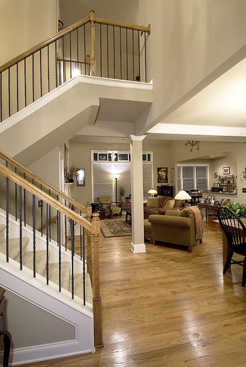 Interior view showing a two-story foyer with a wood-railed staircase, open to a living area with a fireplace and dining space.