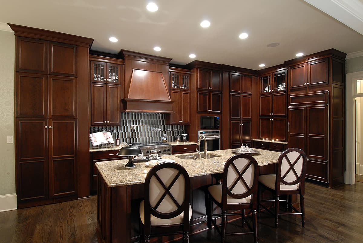 Kitchen with dark wood cabinetry, granite island with seating, range with wood hood, and stainless steel appliances.