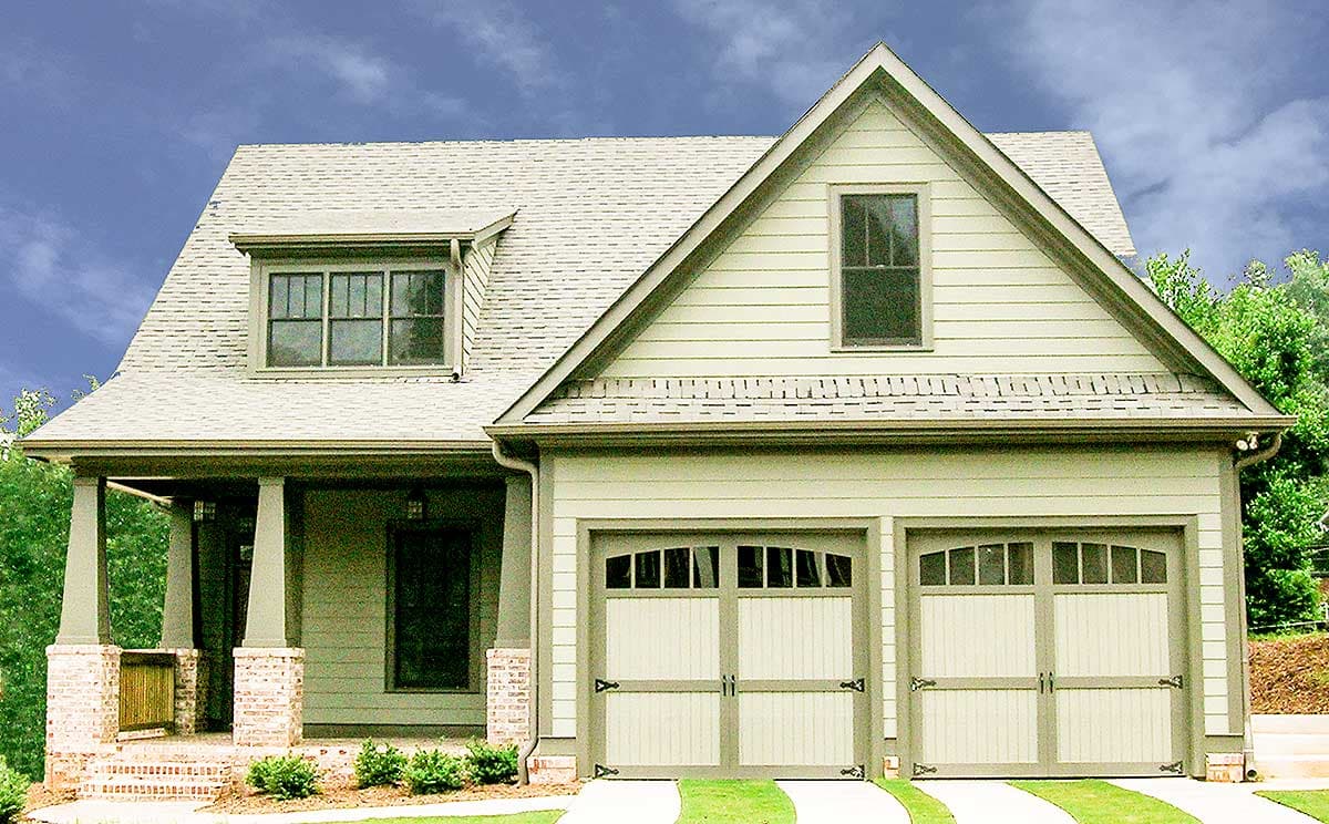 House plan exterior. Craftsman-style home with gabled roof, dormer, and attached garage. Features a covered porch with brick and wood accents.