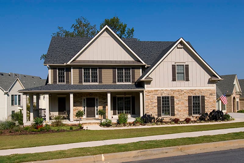House plan exterior. Two-story Colonial-style home with gabled roof, stone facade, covered porch, and multiple shuttered windows.