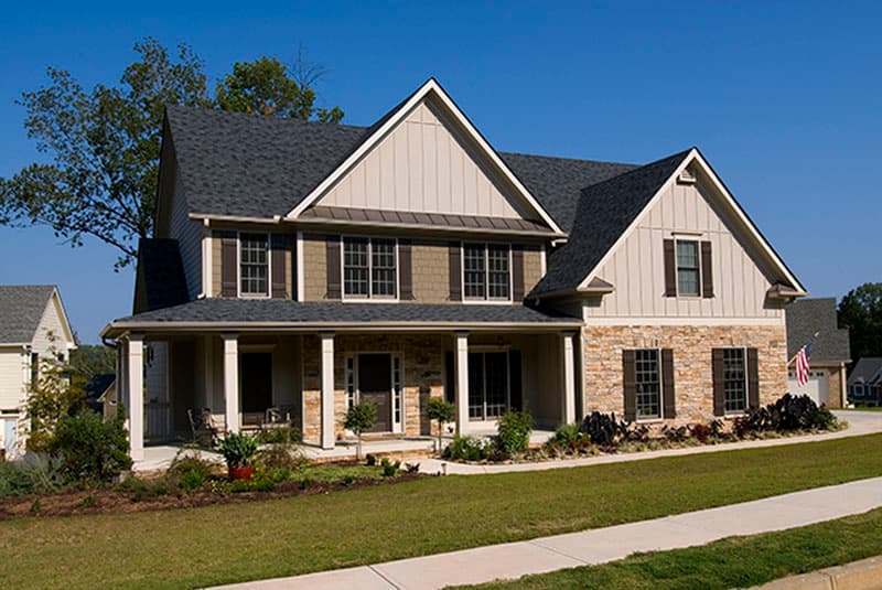 Two-story Modern Farmhouse exterior with stone accents, a wraparound porch, and prominent gables.