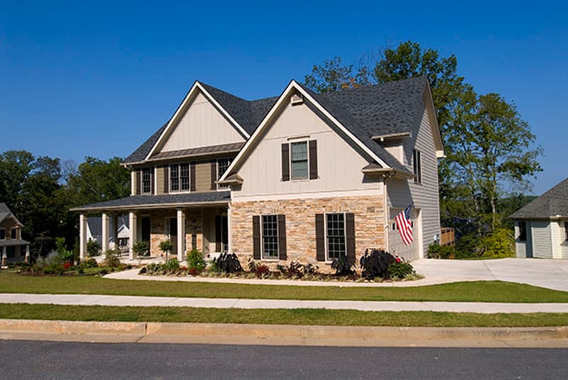 Two-story house plan exterior with stone facade, gabled dormers, wrap-around porch, and attached garage.