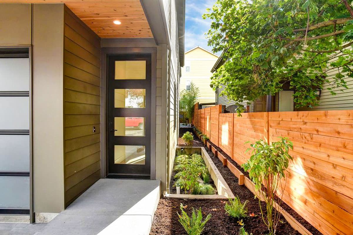 Modern house exterior with horizontal siding, a four-lite entry door, concrete walkway, and wood fence.