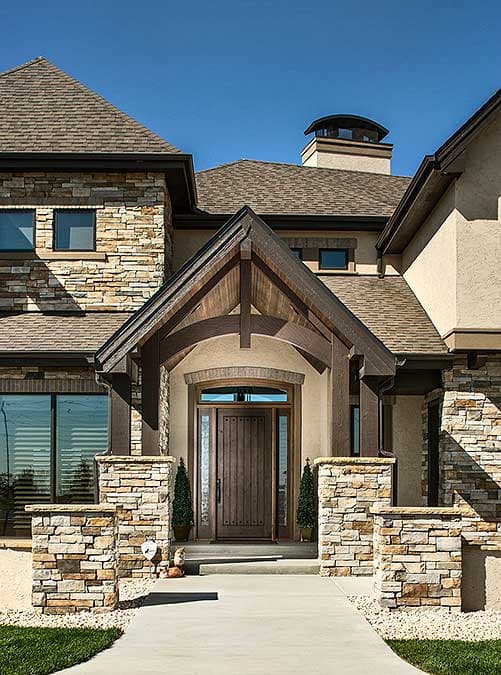 House plan exterior with stone and stucco facade, covered entry with wooden beams, gabled roof, and prominent stone chimney.