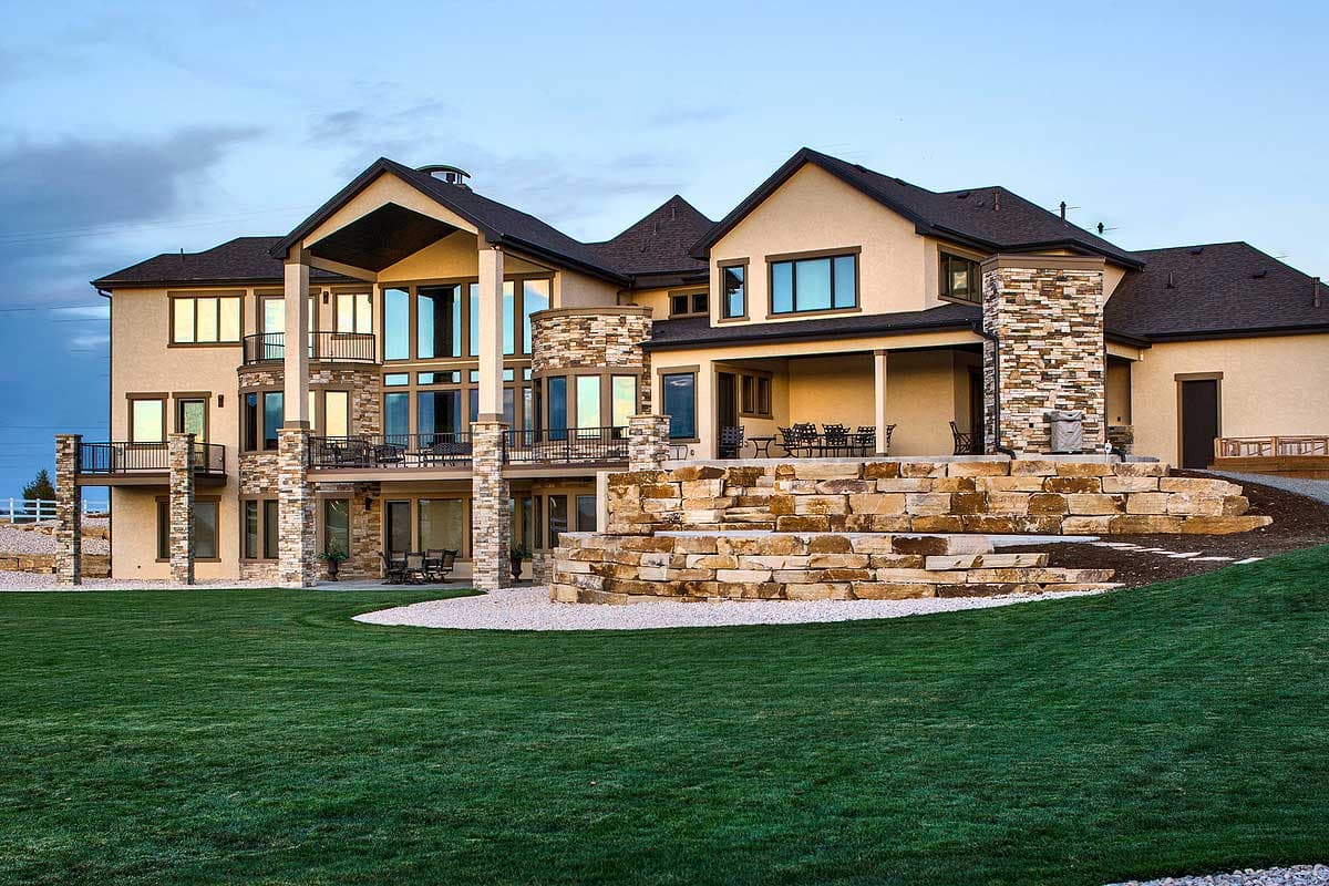 House plan exterior with multiple stories, large windows, covered patios, stone accents, and terraced landscaping.