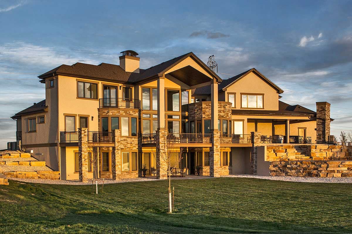House plan exterior featuring multiple stories, stone accents, numerous balconies, and a grand covered entrance.