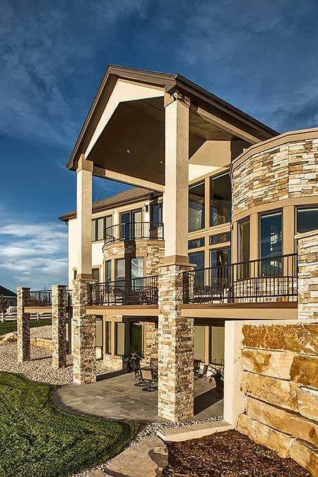 House plan exterior features multiple stories, stone-clad columns, extensive balconies, and large windows.