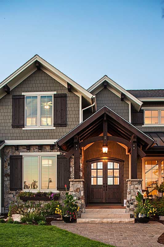 House plan exterior: two-story home with stone and shake siding, prominent gables, dormers, and a covered entry with double wood doors.