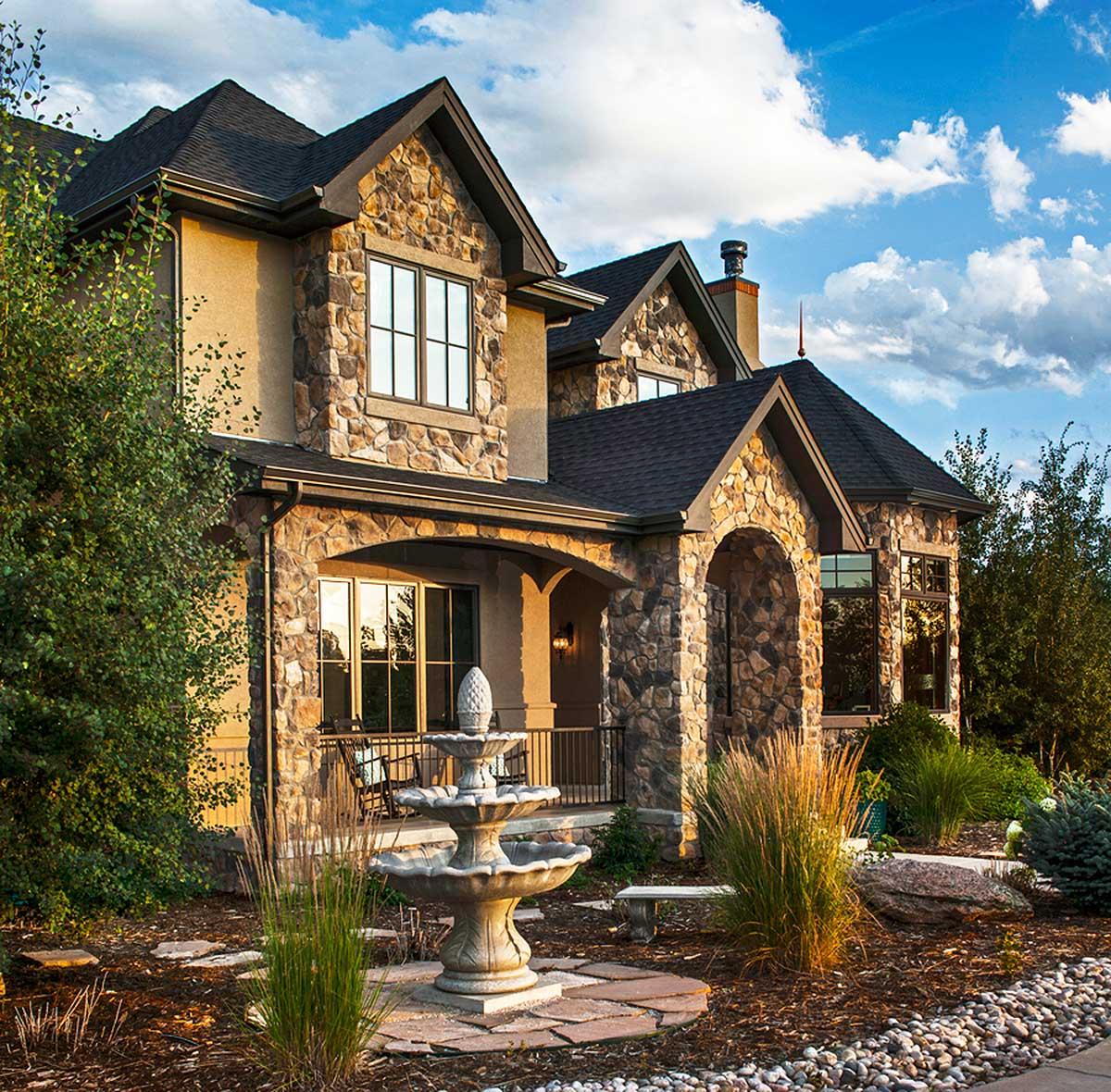 Two-story house plan exterior with stone facade, gabled dormers, arched entryway, and covered porch with fountain.
