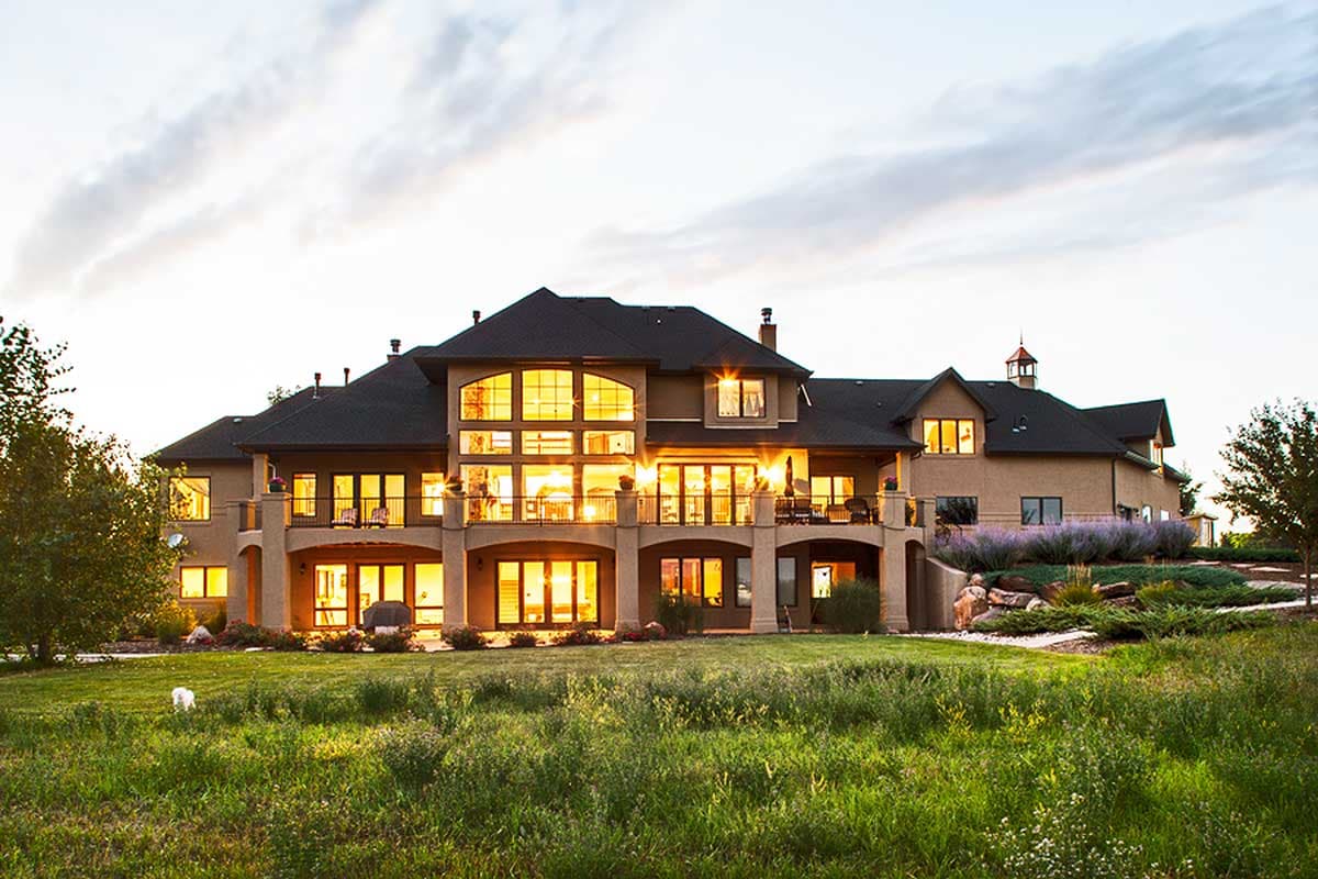 House plan exterior: sprawling tan residence with multiple levels, grand entryway, expansive windows, and covered balconies.