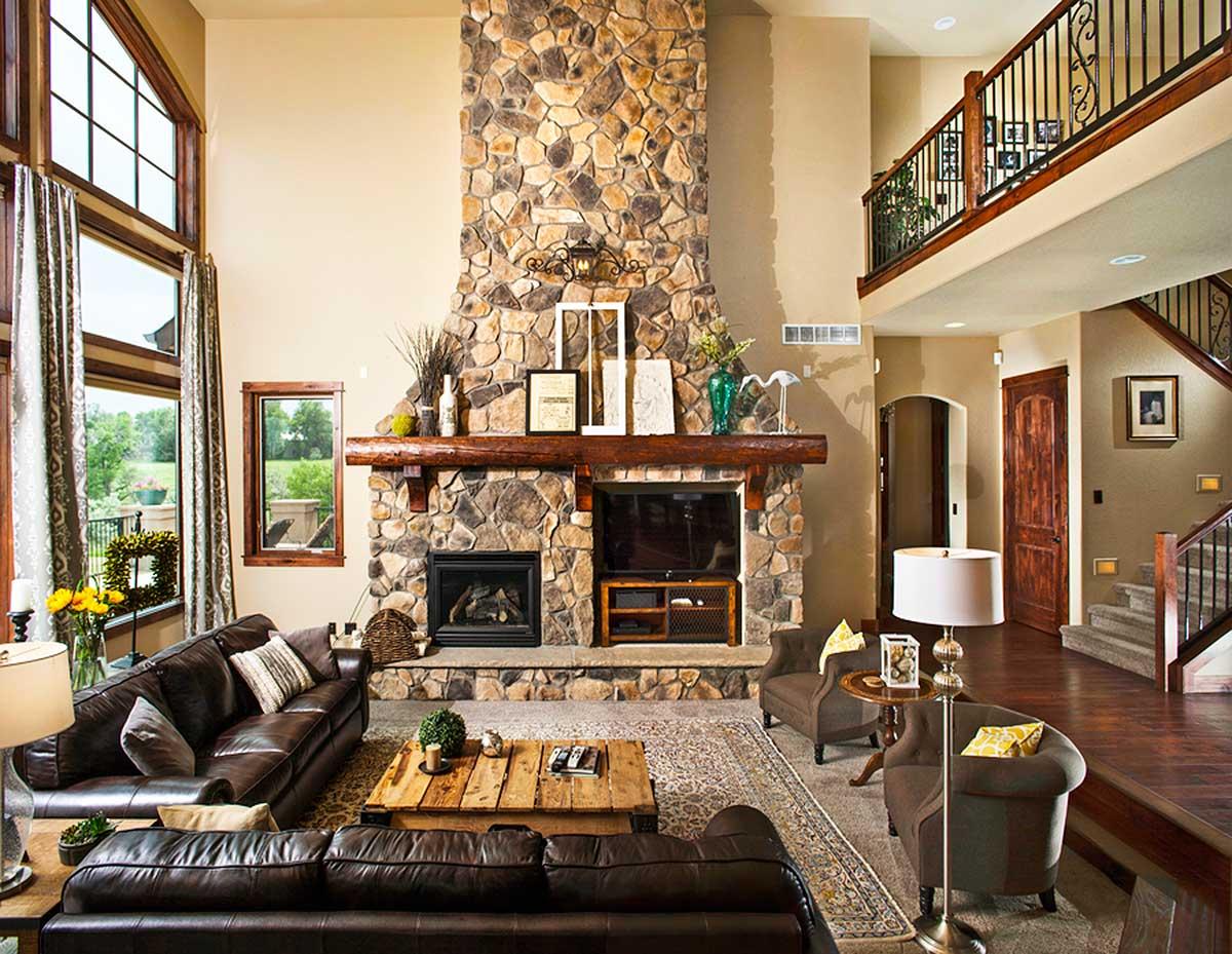 Interior view of a great room with a tall stone fireplace, vaulted ceiling, large windows, and a balcony overlook.