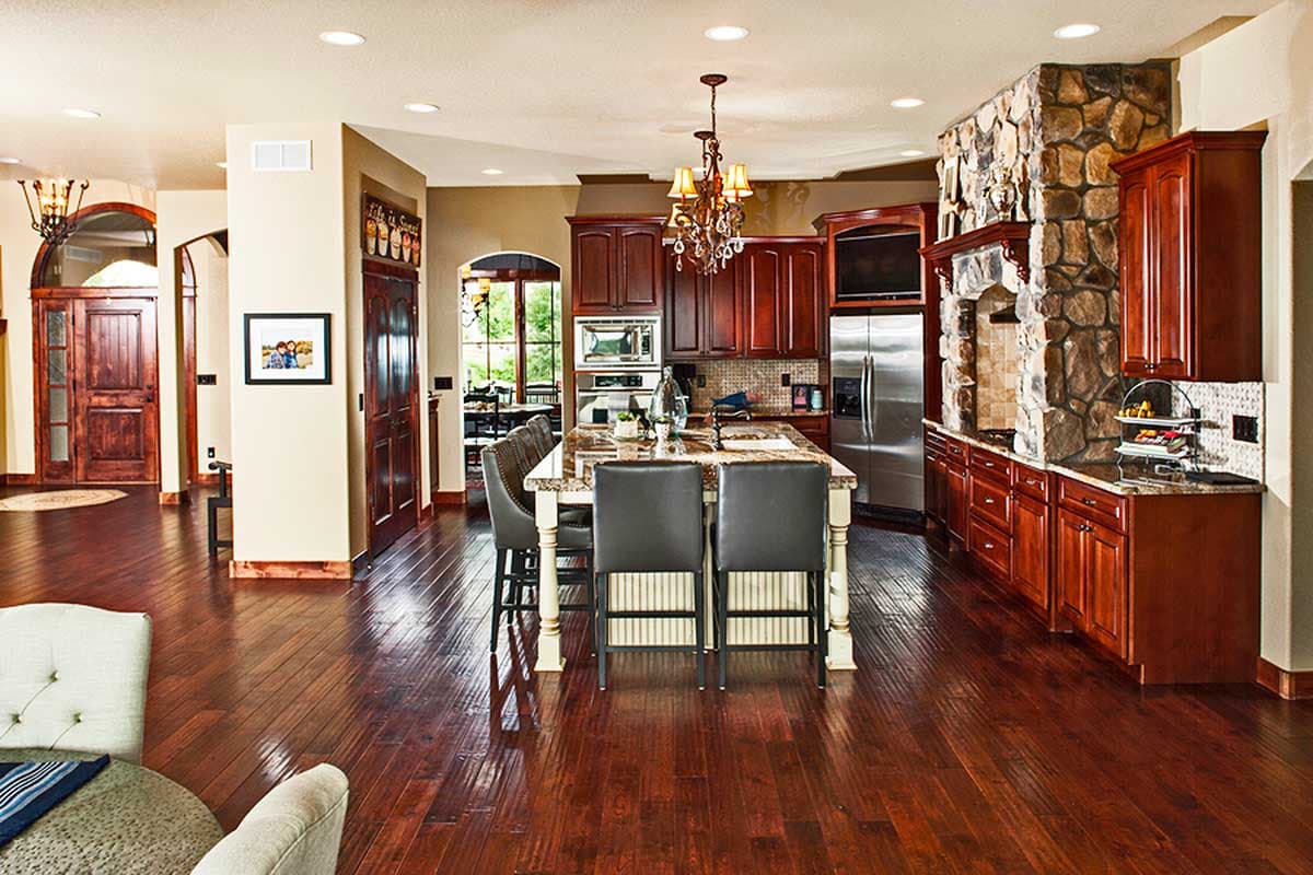 Open-concept kitchen with large island, dark wood cabinets, stone fireplace surround, and stainless steel appliances.