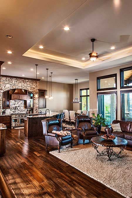 Open concept living area with stone accent wall, kitchen island, leather seating, and coffered ceiling with recessed lighting.