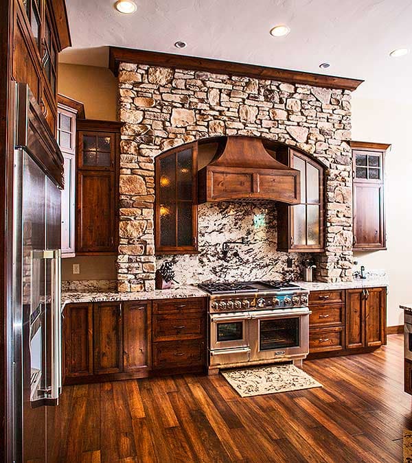 Kitchen with rustic stone range hood, custom wood cabinetry, granite countertops, stainless steel range, and hardwood flooring.