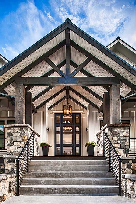 Modern Farmhouse house plan exterior with stone accents, a covered entryway with exposed beams, and a central glass door.