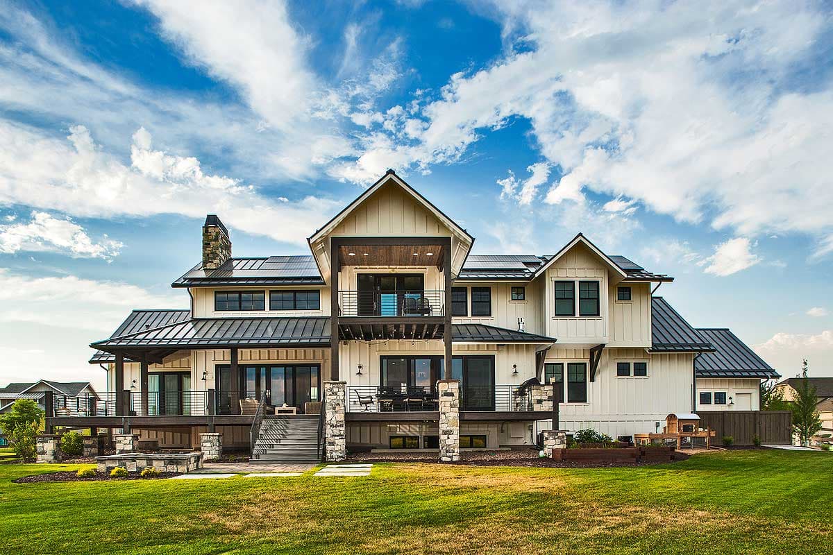 Modern farmhouse house plan exterior with metal roof, stone chimney, multiple gables, and tiered decks.
