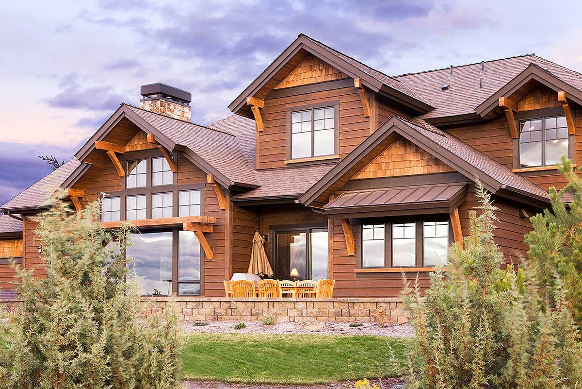 Craftsman style house plan exterior with wood siding, stone chimney, gables, dormers, and large windows.