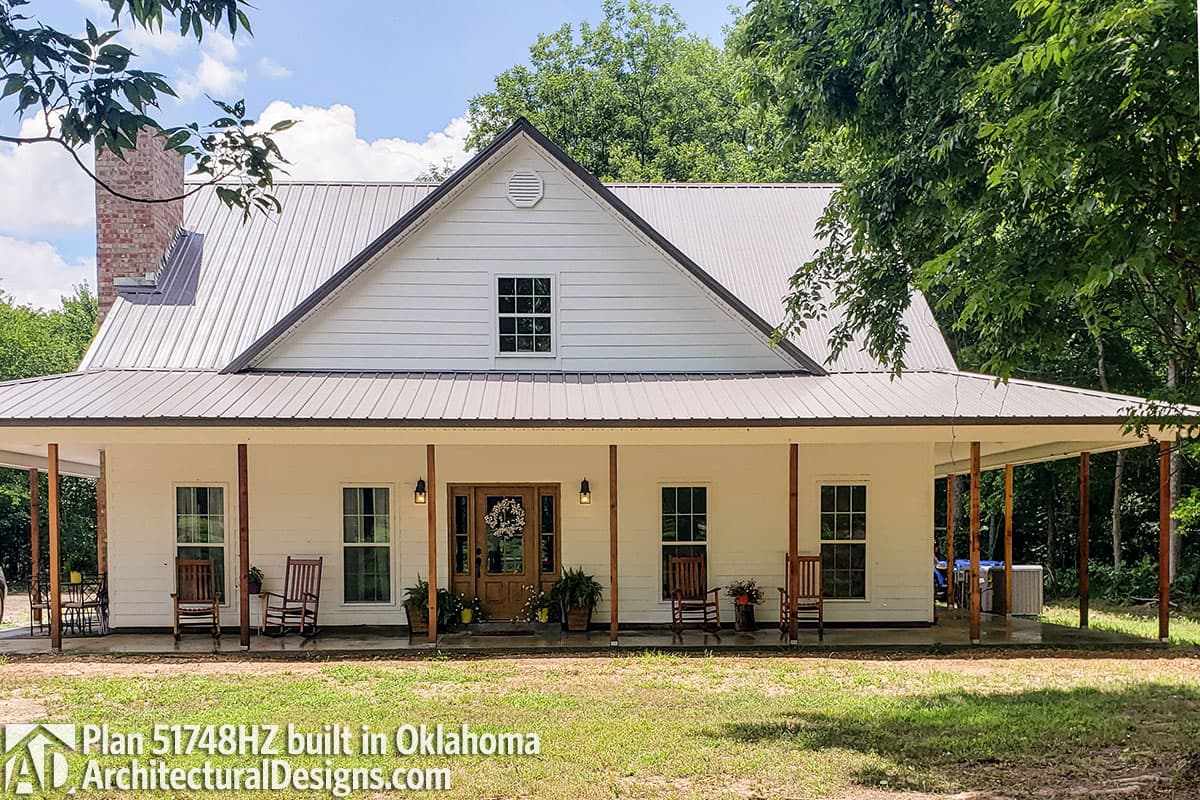 Modern Farmhouse plan exterior with metal roof, wraparound porch supported by wooden posts, and a brick chimney.