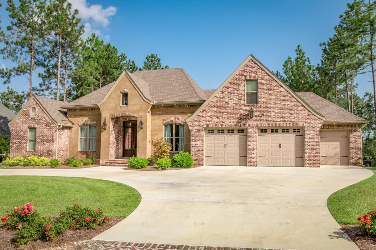 House plan exterior: One-and-a-half story home with arched entry, brick accents, steep gables, and a three-car garage.