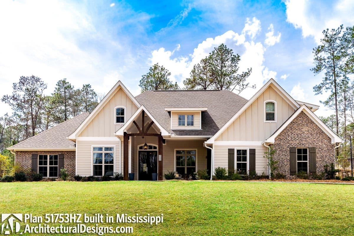House plan exterior: Modern Farmhouse style, two stories, with gabled dormers, exposed wood beams over entrance, and brick accents.