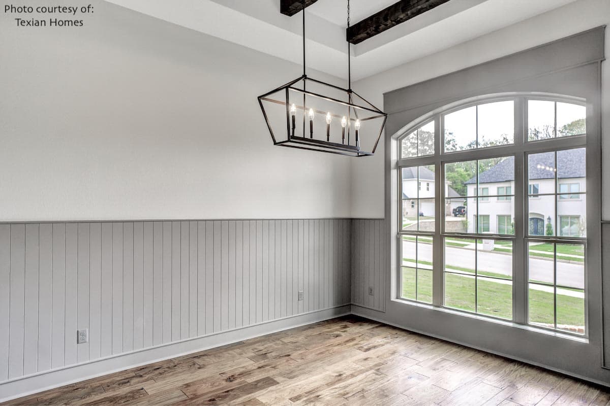 Interior view of a room with beadboard wainscoting, coffered ceiling with wood beams, and a large arched window.