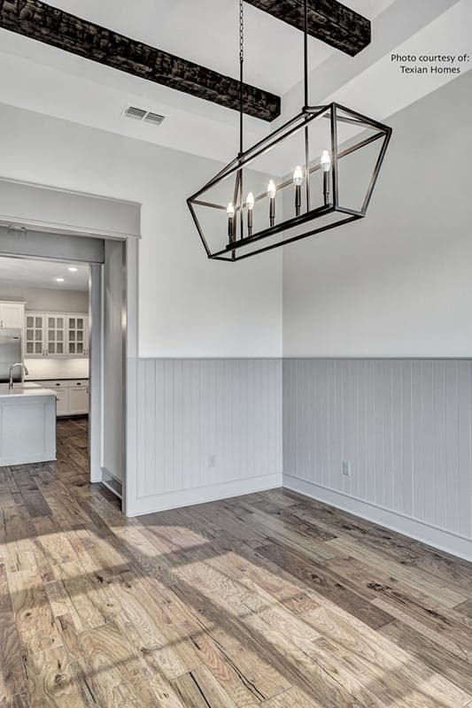Interior view of a dining area with exposed beams, a geometric chandelier, beadboard wainscoting, and hardwood floors.