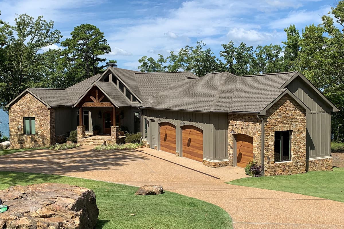 House plan exterior featuring stone accents, a prominent gabled entrance with exposed wood beams, and a three-car garage.