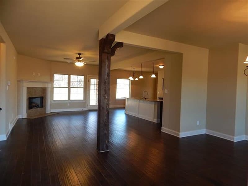 Interior view of a living room with a fireplace, open to a kitchen with an island. Features a decorative wooden beam support.