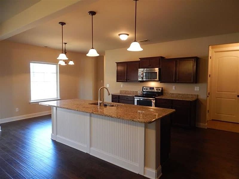 Kitchen with large island, granite countertops, dark wood cabinets, stainless steel appliances, and pendant lighting.