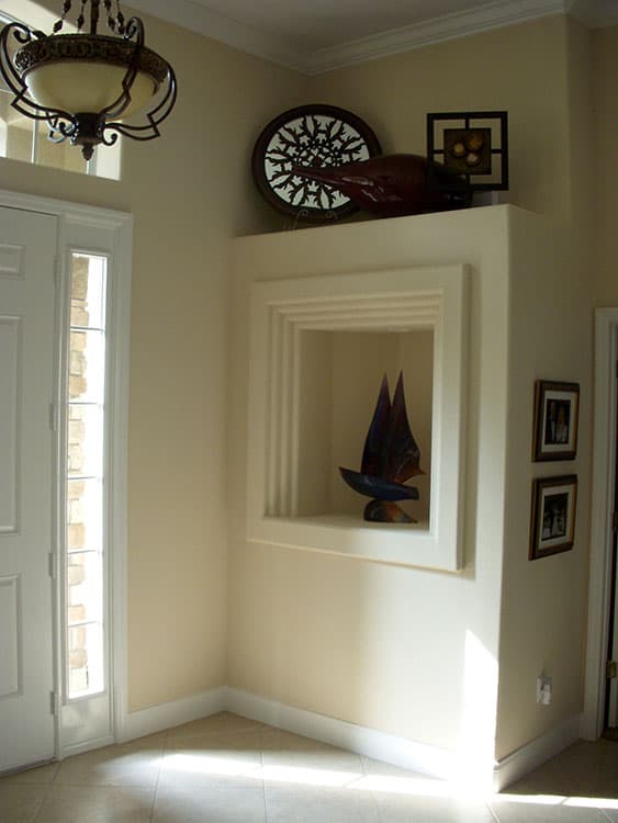 Interior view of entryway with paneled door, chandelier, decorative niche with sculpture, and artwork.
