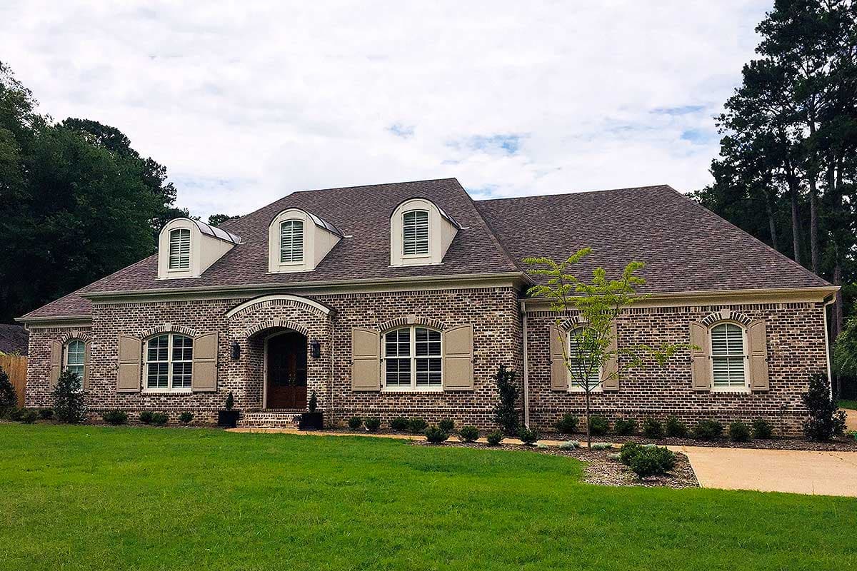 House plan exterior: Brick, one-story, with arched entry, dormers, and louvered shutters.