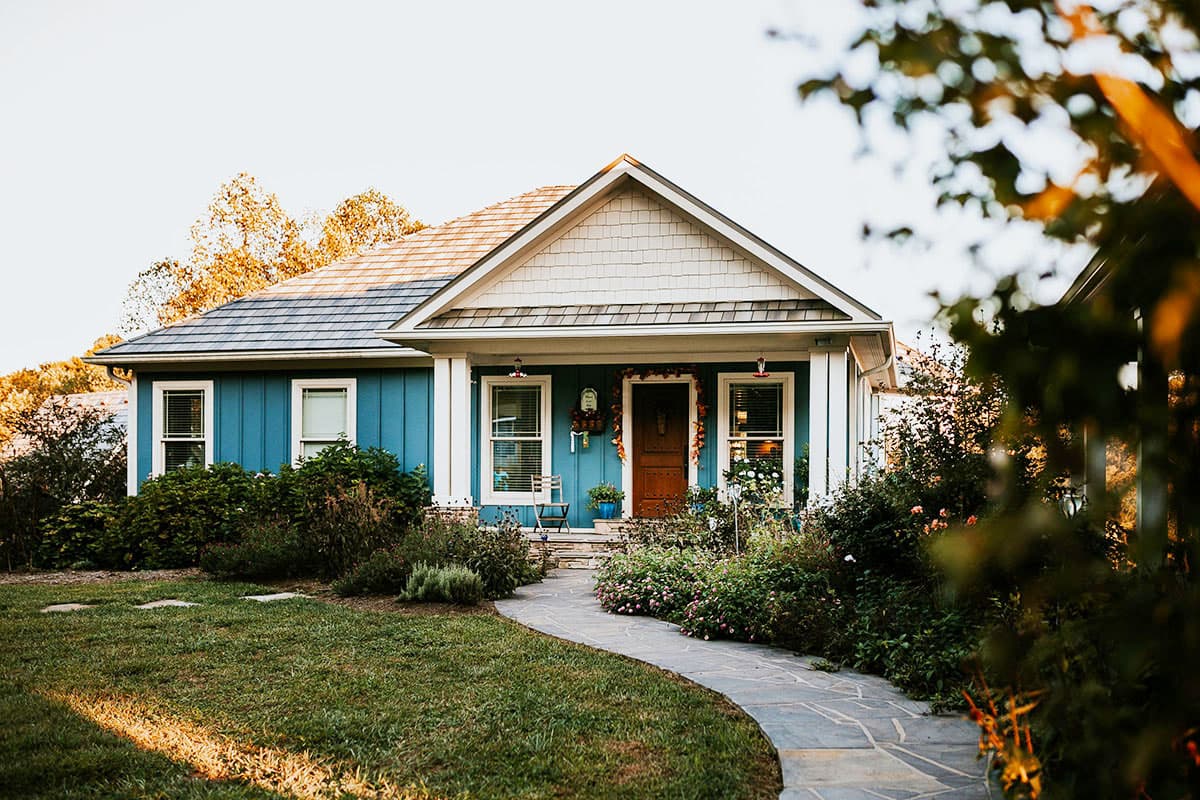 House plan exterior. One-story Cottage style home with gabled roof, front porch, and vertical siding. Stone path leads to the front door.