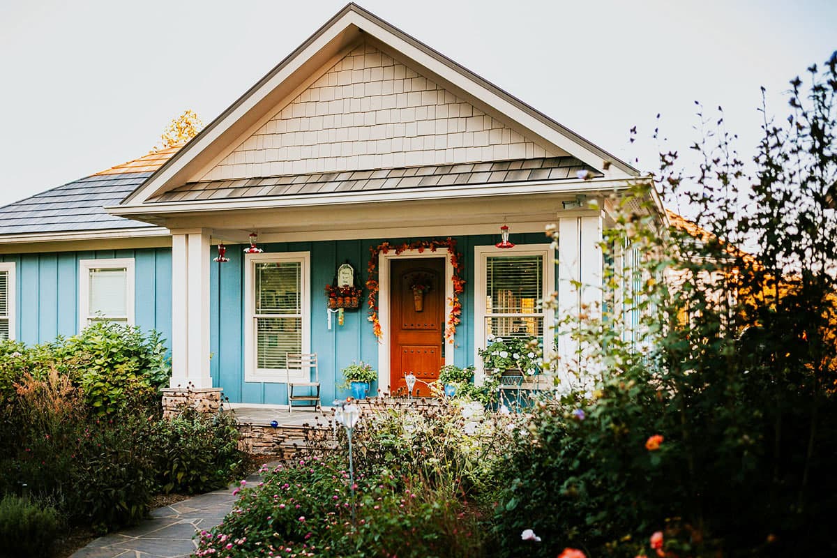 House plan exterior with a covered porch, gable dormer, and stone foundation.