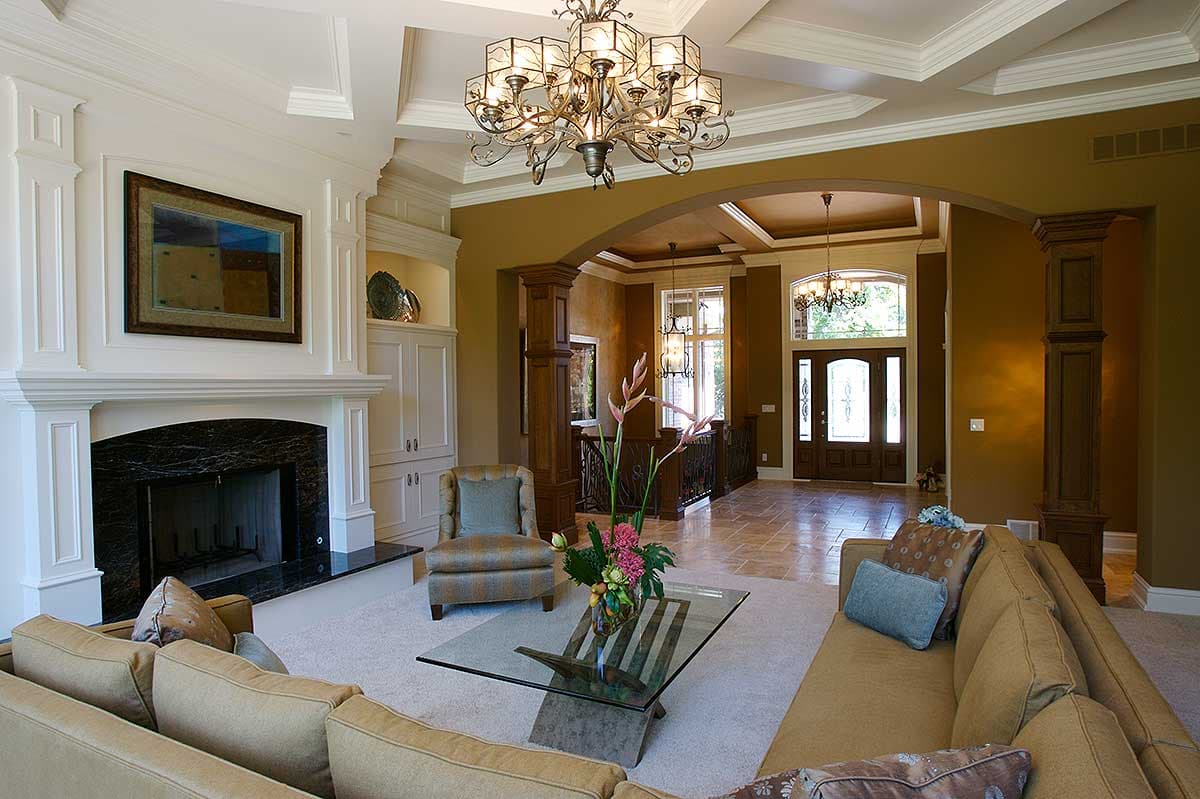 Interior view of a great room with a fireplace, coffered ceiling, and view of the entryway.