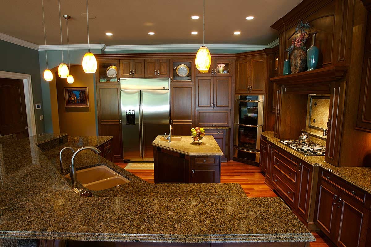 Kitchen with dark wood cabinets, granite countertops, stainless steel refrigerator, island with sink, and gas range.