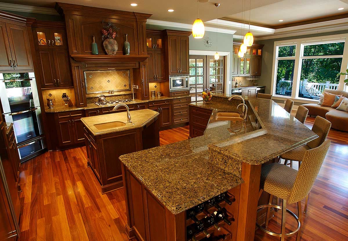 Spacious kitchen with dark wood cabinets, granite countertops, double ovens, island with sink, and bar seating.