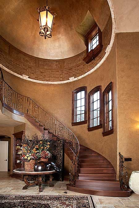 Interior view of a curved staircase with ornate metal railings, wood treads, and a domed ceiling with brick accent.