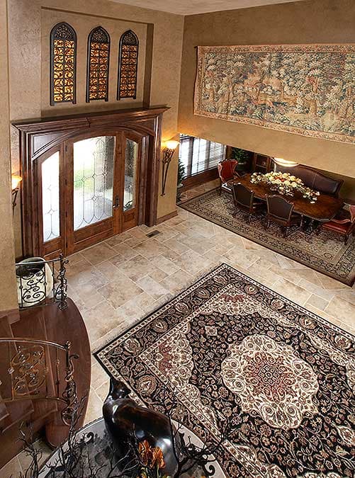 Interior view of a foyer with double wooden doors, ornate metalwork windows, a tapestry, and a dining area visible beyond.