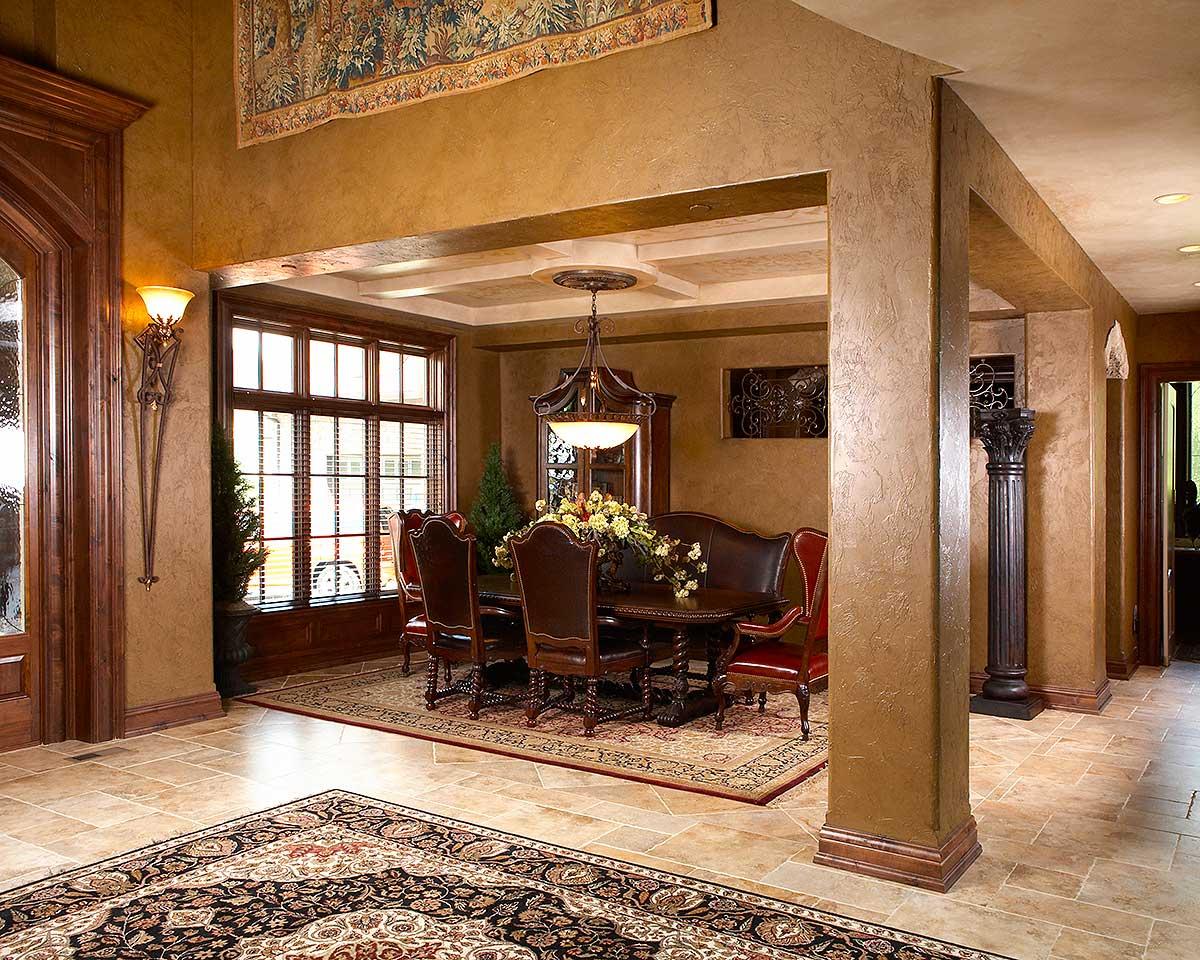 Dining room with large bay window, ornate chandelier, wooden table and chairs, and decorative wall tapestry.