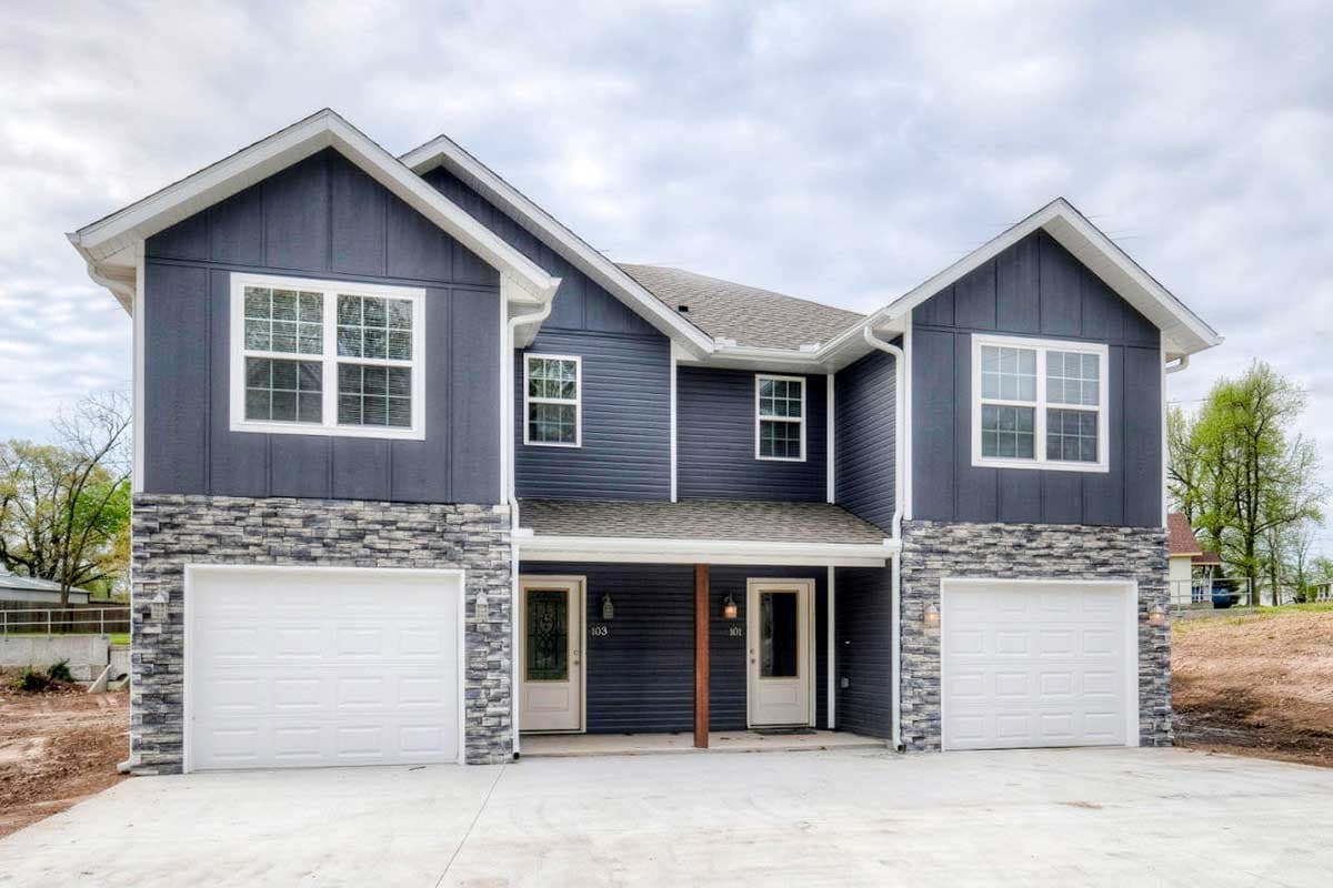 House plan exterior: Two-story duplex with board and batten siding, stone base, gables, and two single-car garages.